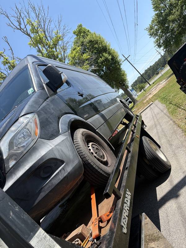 Black Sprinter-style van loaded on a flatbed, seen from a low angle