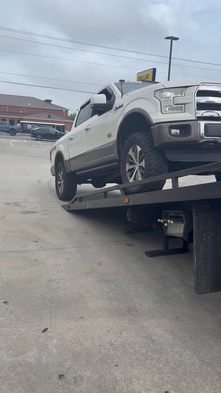 White lifted pickup sitting on a tilted flatbed bed in a parking lot