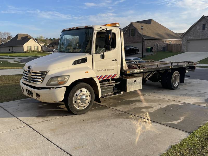White cab-over flatbed tow truck parked in a subdivision with an empty bed